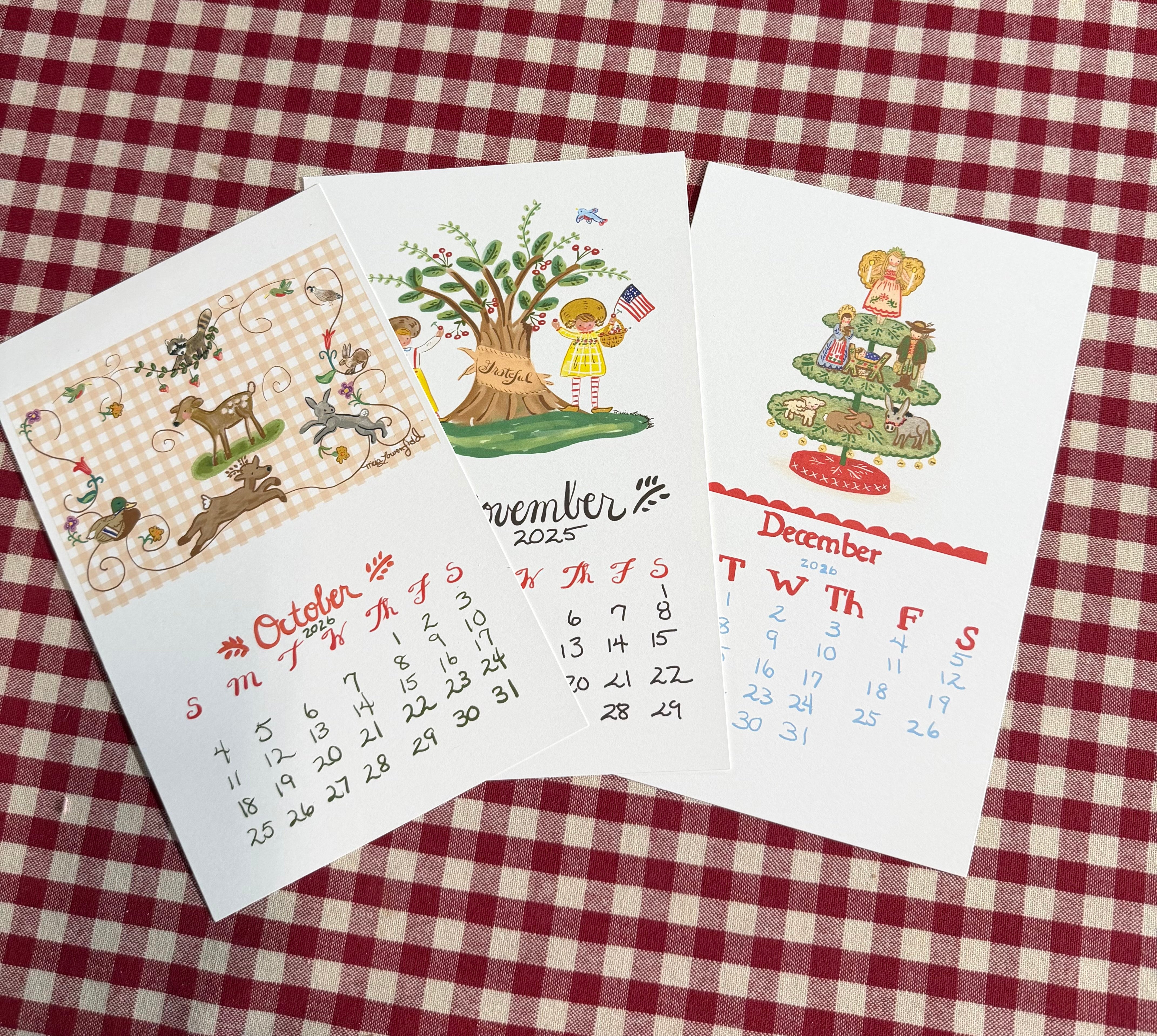 Three pages of a calendar for October, November, and December 2025 on a red and white checkered tablecloth.
